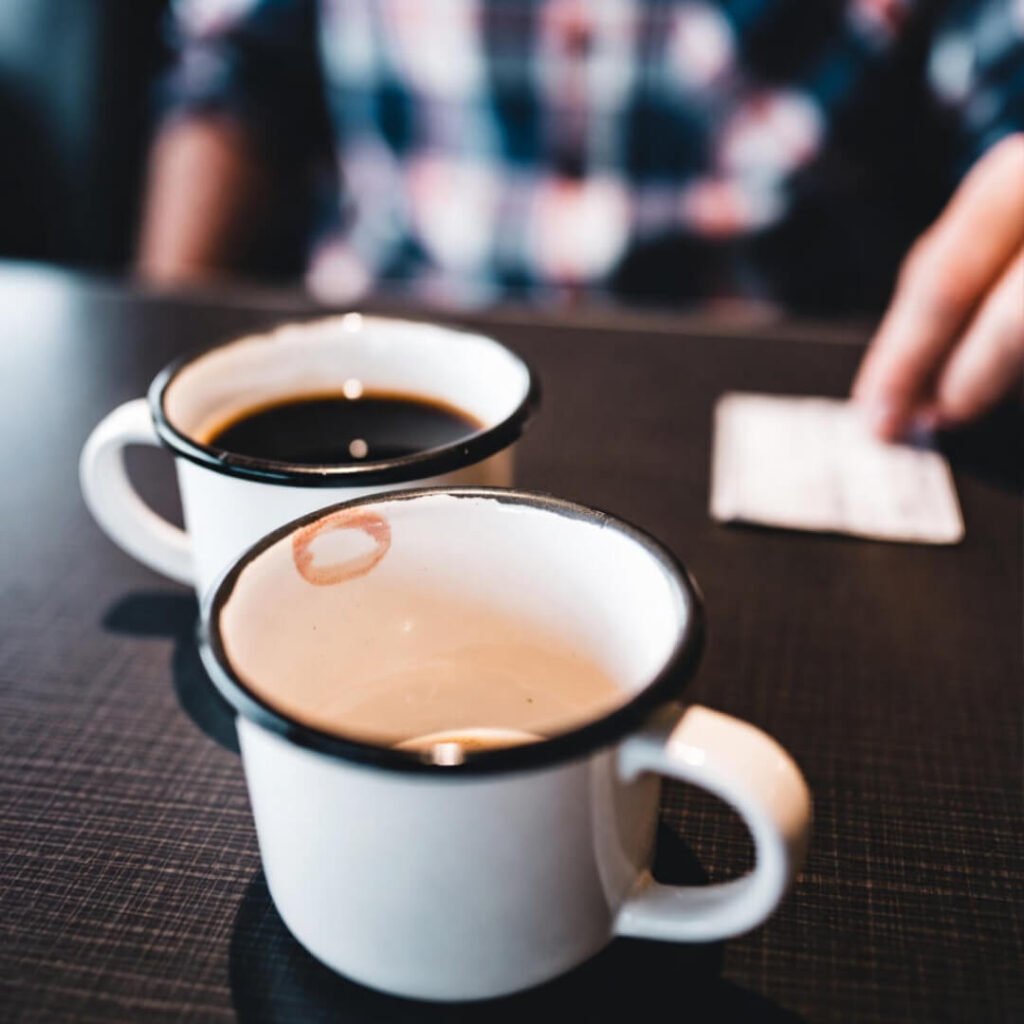Two diner coffee cups, one full, one half-empty with lipstick; hand grabs check in blur.