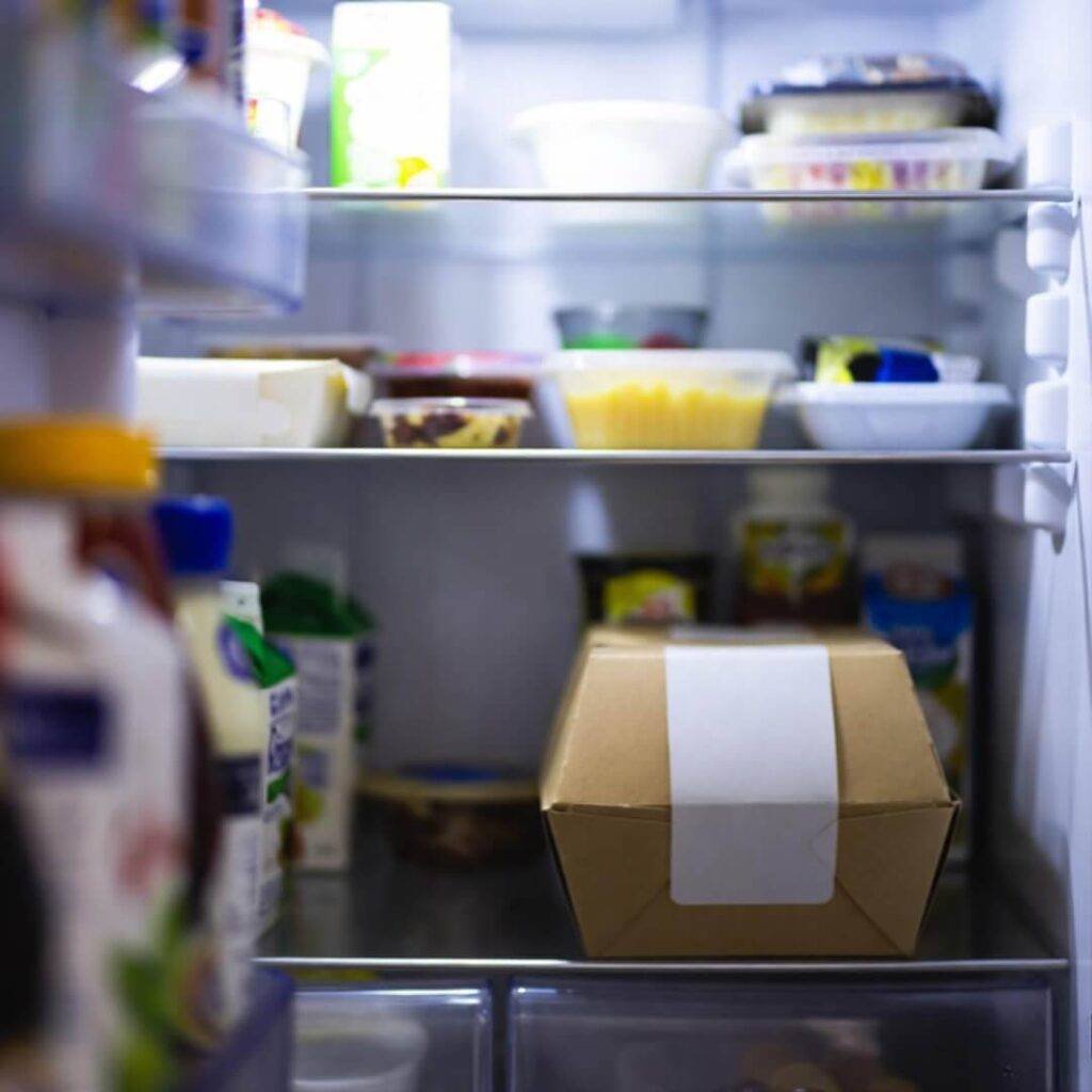Sneaky over-shoulder view of open fridge with two untouched takeout containers.