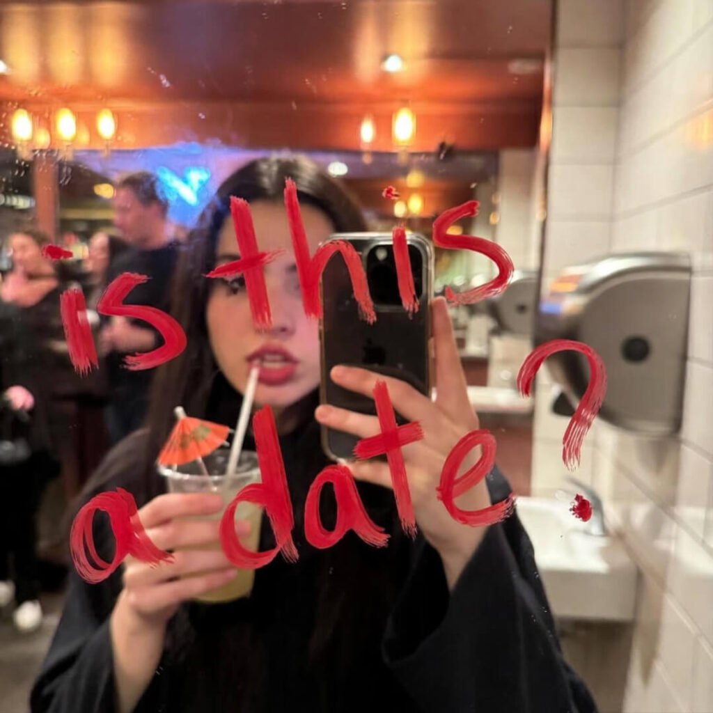 Blurry bar bathroom mirror selfie, smudged mascara, umbrella drink, “is this a date?” in lipstick.